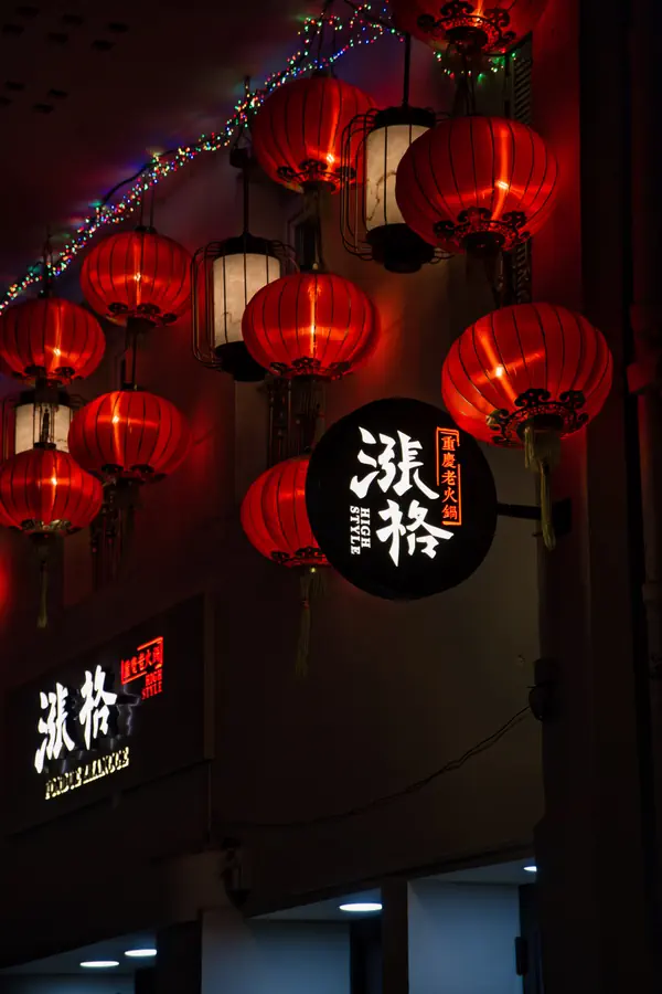 Devanture d'un restaurant asiatique décorée de lanternes chinoises rouges traditionnelles et d'enseignes lumineuses avec des caractères chinois, le tout souligné par une guirlande multicolore créant une ambiance chaleureuse et festive dans la nuit.