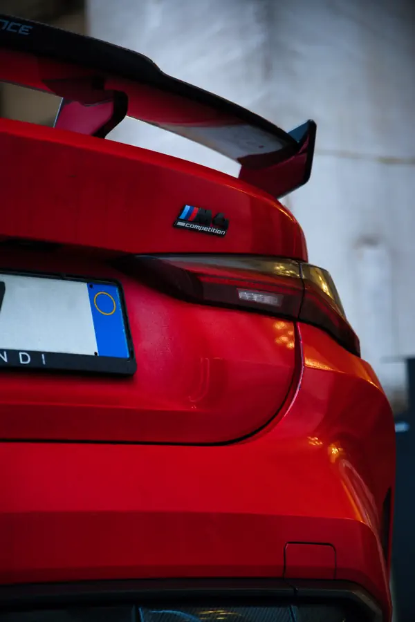 Détail de l'arrière d'une BMW M Competition orange vif, montrant le badge M Competition et une partie de l'aileron arrière.