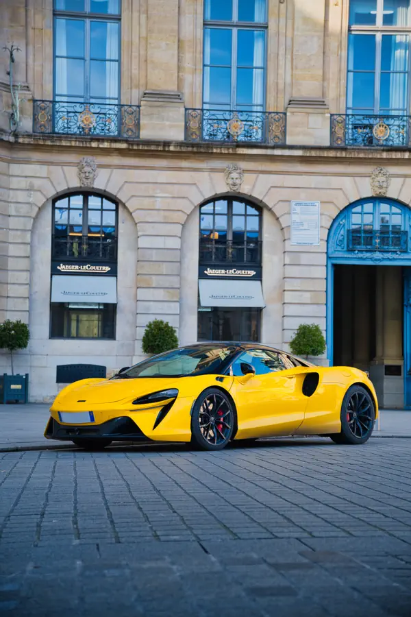 McLaren Artura jaune stationnée devant une boutique Jaeger-LeCoultre. La supercar se distingue par ses lignes aérodynamiques, ses jantes noires, ses étriers de frein rouges et sa silhouette caractéristique avec ses prises d'air latérales.