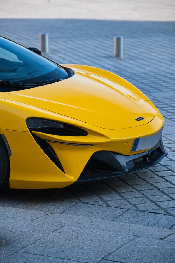 Détail de l'avant d'une McLaren Artura jaune, mettant en évidence le design aérodynamique de son museau avec ses phares effilés, ses entrées d'air sculptées et son splitter avant en fibre de carbone.