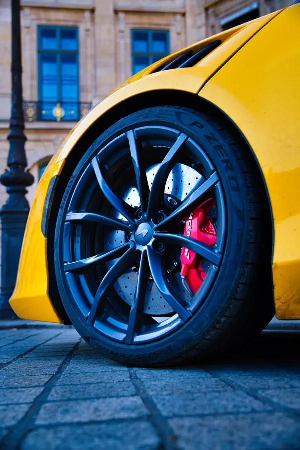 Gros plan sur la roue avant de la McLaren Artura, montrant une jante en alliage gris anthracite au design sportif à dix branches, un étrier de frein rouge vif et un disque de frein perforé.