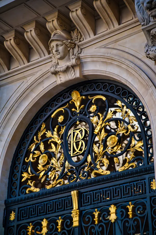 Détail architectural d'une porte d'entrée parisienne ornementée, avec une grille en fer forgé peinte en bleu foncé et décorée de motifs floraux dorés.