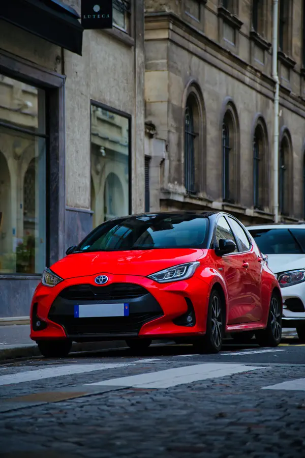 Toyota Yaris hybride rouge de dernière génération, photographiée de trois-quarts avant dans une rue parisienne.