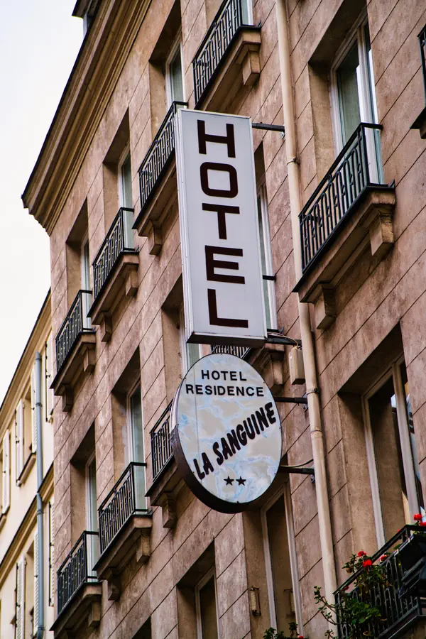 Enseigne d'hôtel sur une façade parisienne avec un panneau vertical blanc indiquant "Hôtel Résidence La Sanguine" sur un bâtiment en pierre avec balcons en fer forgé.