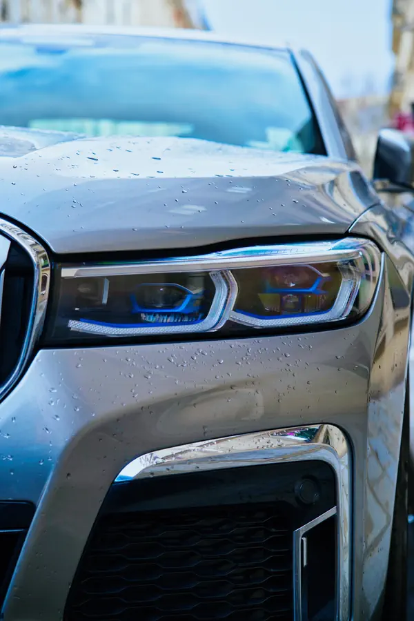 Gros plan sur le phare avant d'une BMW série 7 avec sa signature lumineuse LED caractéristique en forme de L et ses détails bleus distinctifs.