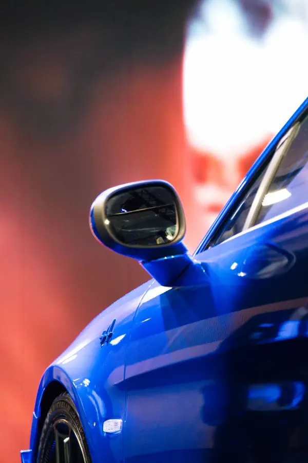 Détail du rétroviseur et de l'aile avant d'une Alpine bleue, mettant en valeur le logo "A" sur une carrosserie aux reflets brillants.