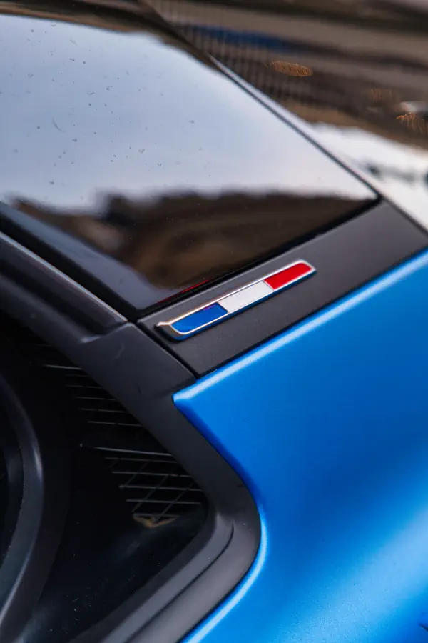 Détail du drapeau français en badge chromé sur l'aile arrière de l'Alpine A110 bleue.