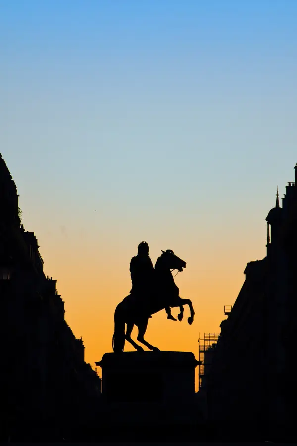 Silhouette d'une statue équestre au lever du soleil, se détachant en ombre noire sur un ciel dégradé d'orange à bleu.
