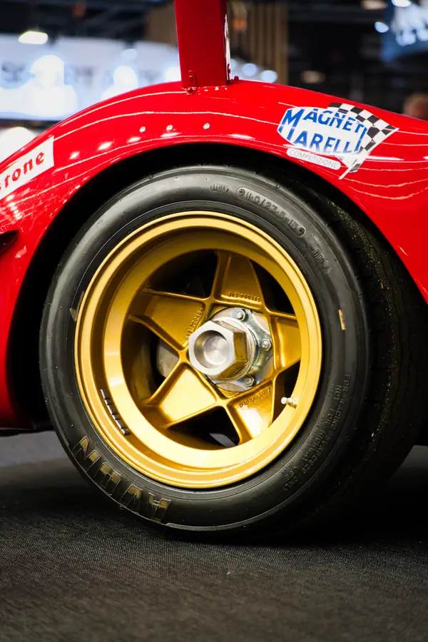 Gros plan d'une jante dorée à cinq branches montée sur une voiture de course rouge, avec pneu Avon et logo Magneti Marelli sur l'aile.