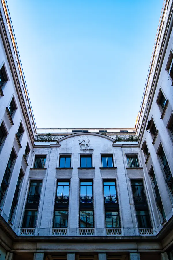 Façade intérieure d'un immeuble Art déco parisien vue depuis une cour, avec ses fenêtres régulières, ses balcons en fer forgé et un bas-relief décoratif au sommet représentant une figure en mouvement.