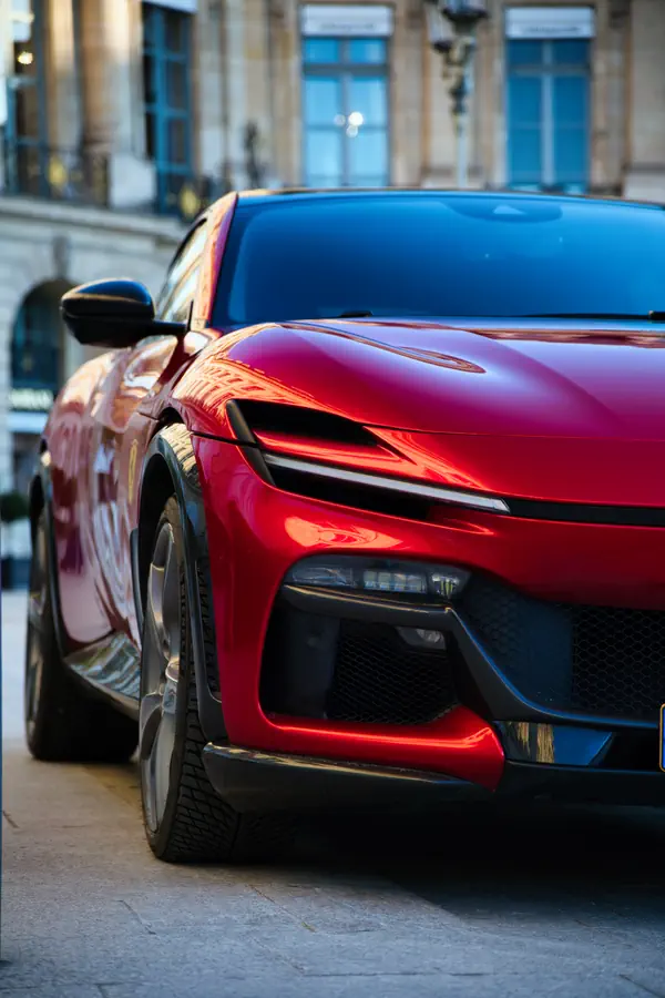 Détail de l'avant d'une Ferrari Purosangue rouge, montrant son design agressif avec ses phares effilés, ses grandes prises d'air et son bouclier avant sculptural.