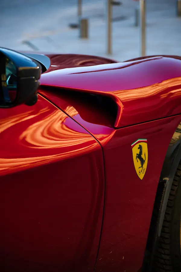 Détail de l'aile avant d'une Ferrari Purosangue rouge avec l'emblématique écusson Ferrari sur fond jaune.