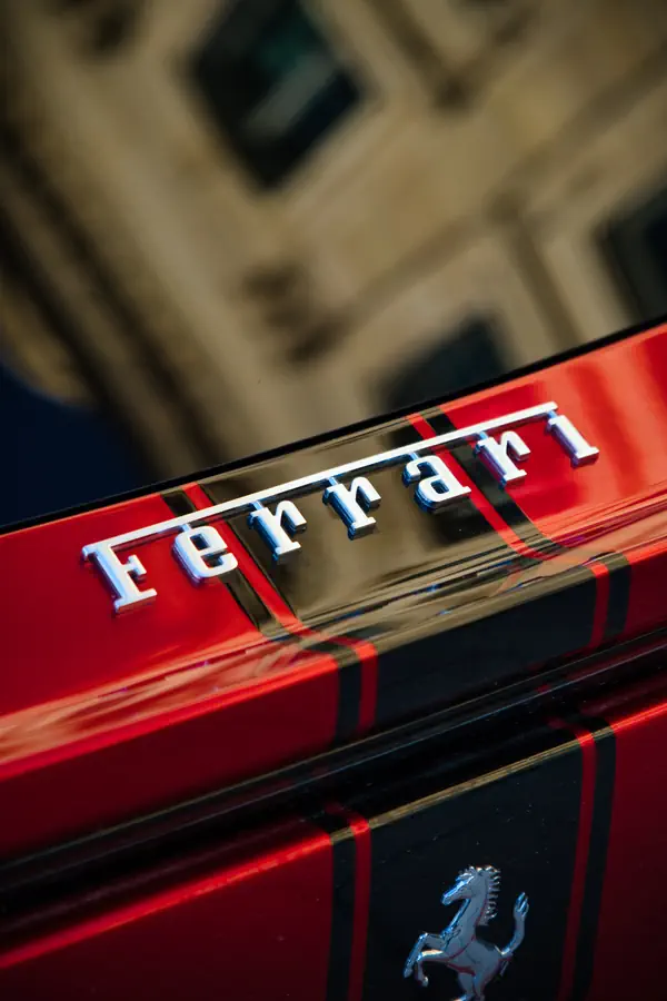 Gros plan sur le badge "Ferrari" en lettres chromées sur la carrosserie rouge d'une Ferrari Purosangue, avec le cheval cabré visible en dessous.