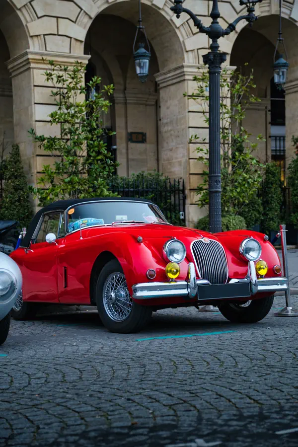 Jaguar XK150 rouge classique garée sous les arcades d'un bâtiment parisien.