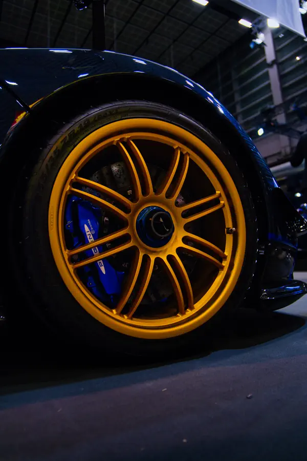Gros plan sur une roue de voiture de sport avec une jante en alliage jaune au design multibranches et un étrier de frein bleu visible derrière.