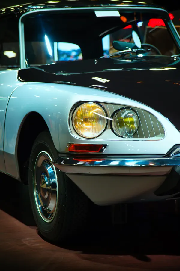 Détail de l'avant d'une Citroën DS classique blanche, montrant ses phares caractéristiques avec le phare jaune antibrouillard typique des voitures françaises de l'époque.