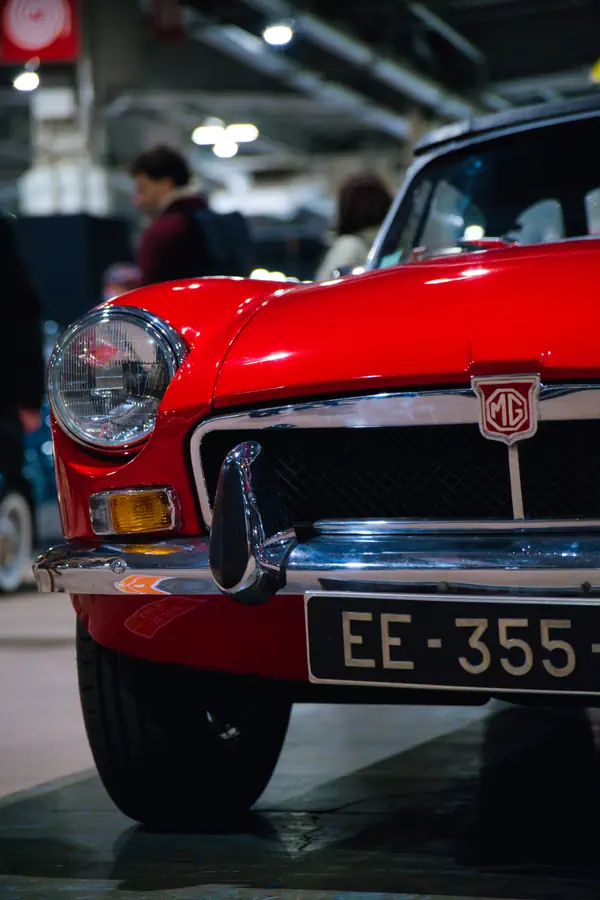 Détail de l'avant d'une MG classique rouge avec son badge octogonal caractéristique, son phare rond, son clignotant orange et sa calandre chromée.