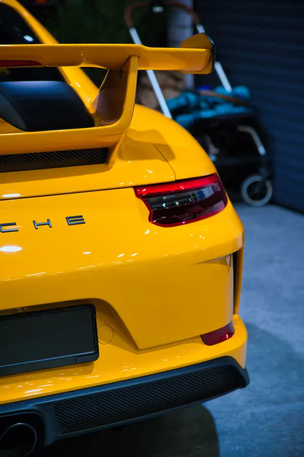Détail de l'arrière d'une Porsche 911 GT3 jaune, montrant son grand aileron fixe, son feu arrière LED caractéristique et sa grille d'aération en nid d'abeille.