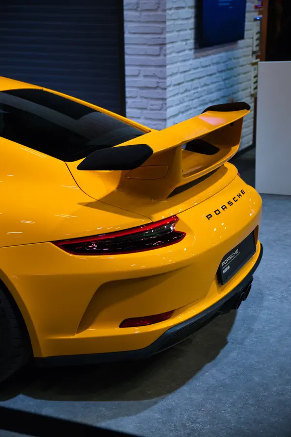 Arrière d'une Porsche 911 GT3 jaune montrant son imposant aileron fixe à double support, ses feux LED caractéristiques en bandeau et le lettrage "PORSCHE" en noir.
