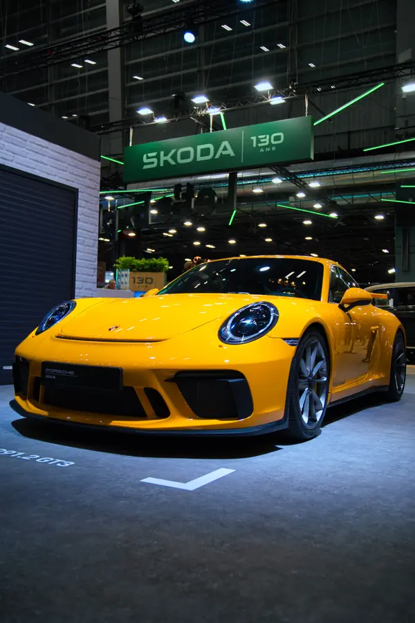 Porsche 911 GT3 jaune exposée dans un salon automobile. La voiture est présentée de trois-quarts avant, mettant en valeur ses phares LED caractéristiques, sa large prise d'air avant et ses lignes aérodynamiques distinctives.