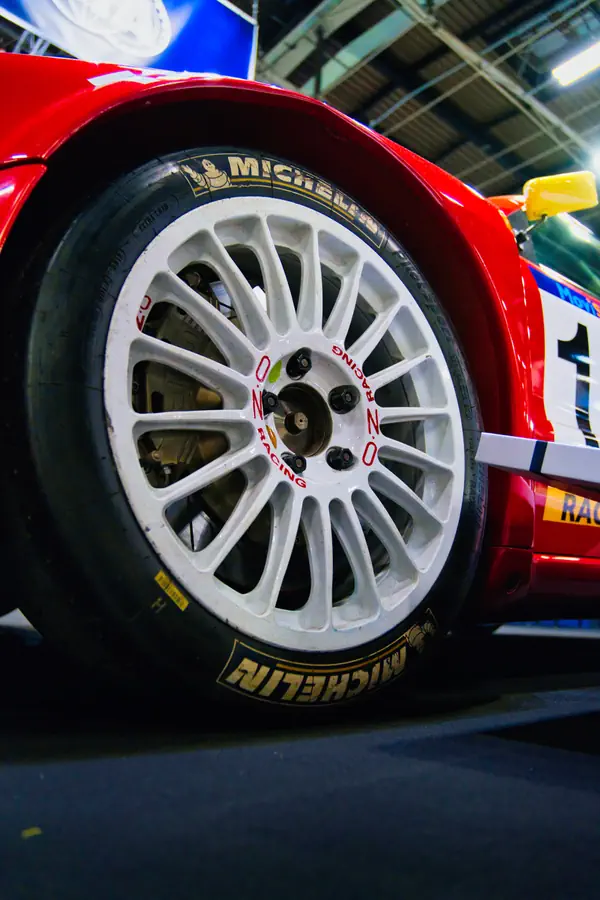 Gros plan sur une roue de voiture de course avec une jante OZ Racing blanche à multiples branches, montée d'un pneu Michelin de compétition.
