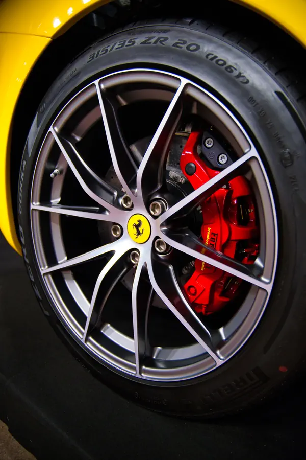 Gros plan sur une roue de Ferrari montrant sa jante en alliage gris à branches multiples avec le logo du cheval cabré au centre et l'étrier de frein rouge caractéristique de la marque.