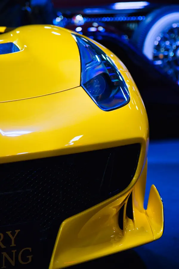 Détail de l'avant d'une Ferrari jaune, montrant le phare LED et une partie du pare-chocs avant avec sa grille noire et son aileron inférieur aérodynamique.