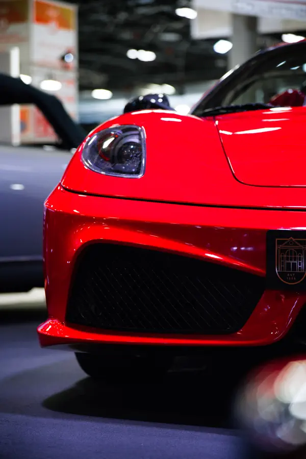 Détail de l'avant d'une Ferrari F430 rouge, montrant son phare triangulaire et sa large grille noire inférieure.