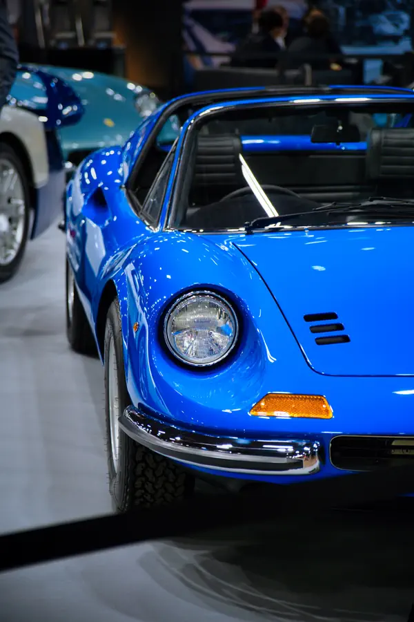 Détail de l'avant d'une Ferrari Dino bleue, montrant son phare rond caractéristique, son clignotant orange et son pare-chocs chromé.