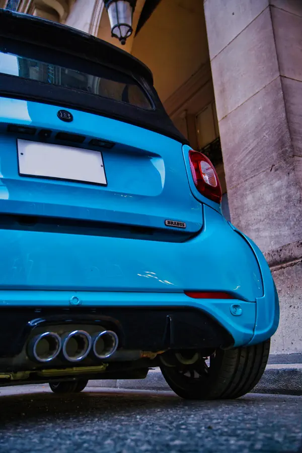 Détail de l'arrière d'une Smart Brabus bleue, montrant ses trois sorties d'échappement caractéristiques, son badge Brabus et son feu arrière.