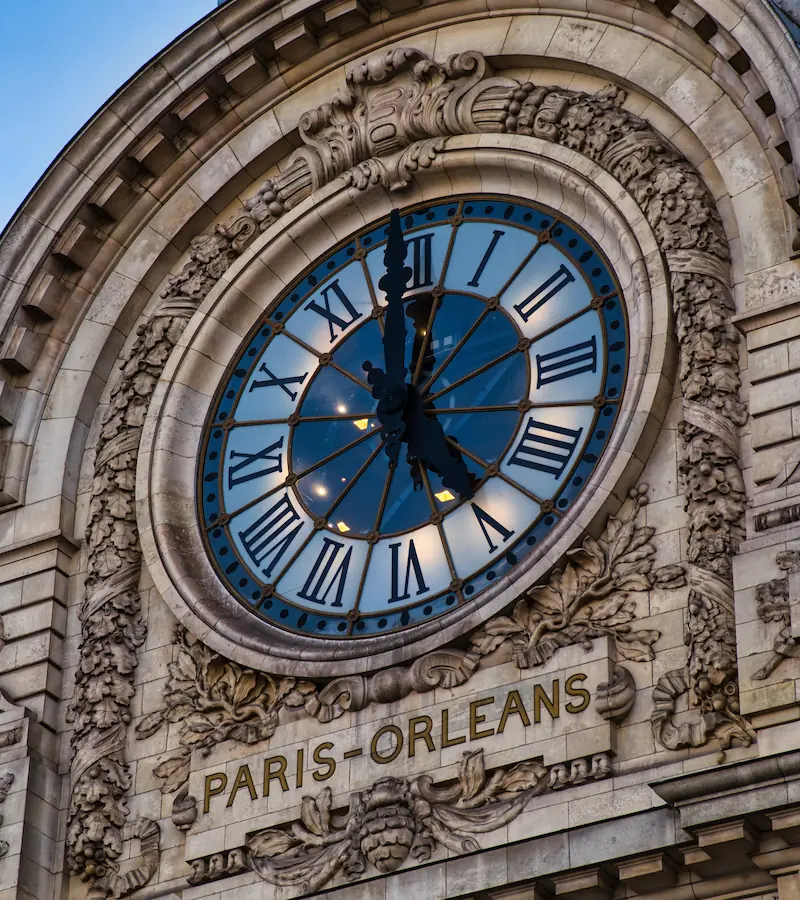 Horloge monumentale du Musée d'Orsay avec son cadran à chiffres romains sur fond bleu, encadrée d'ornements sculptés en pierre.
